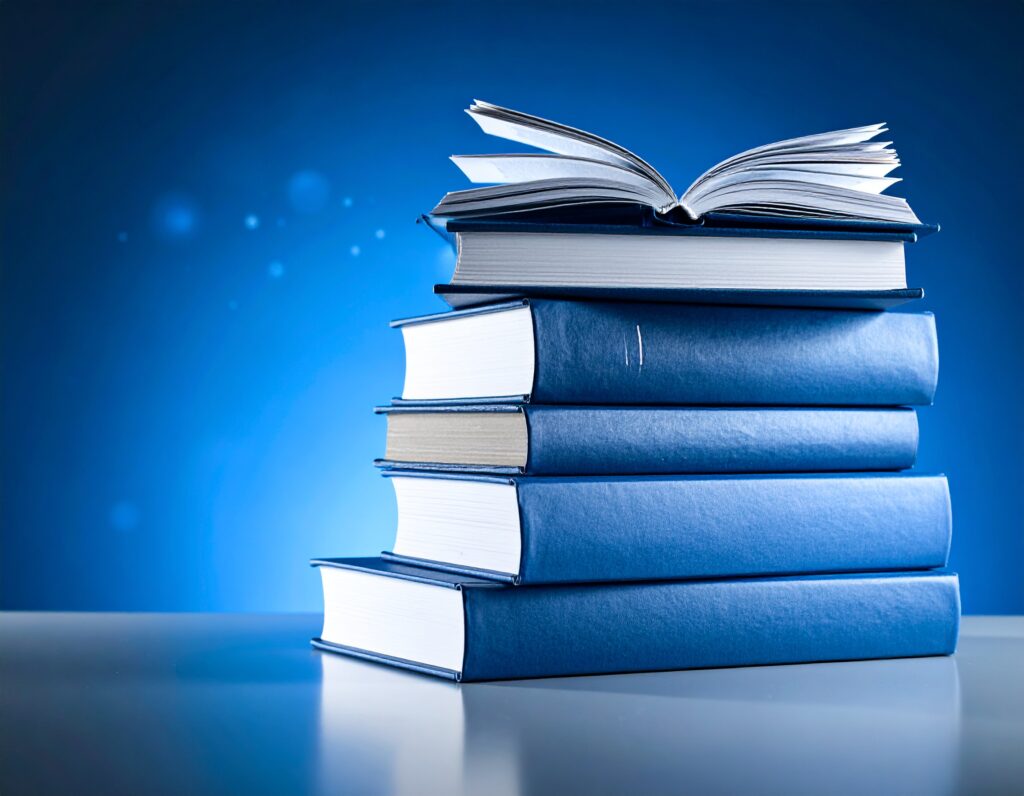 青い背景の前に積まれた5冊の本。一番上の本だけが開かれており、知識や学習の始まりを象徴している。"