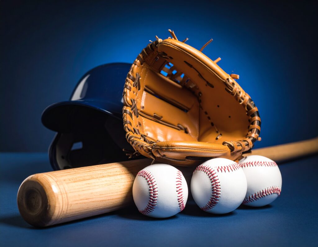 青い背景の前に置かれた野球用具一式。バット、3つのボール、革のグローブ、ヘルメットが写っており、AIのディープラーニングをプロ野球選手の成長に例える記事のテーマを象徴している。